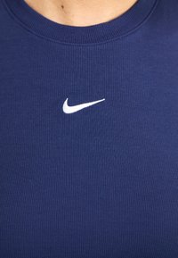 Jūras spēku zilas svītrainas bez piedurknēm blūze ar mazu balto Nike logo uz krūtīm, izgatavota no elastīga materiāla, ar apaļu kakla izgriezumu.