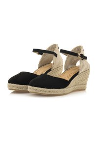 Espadrilles compensées en suède noir avec des sangles en tissu beige texturé, boucle ajustable et semelle intermédiaire en jute. Design à bout fermé.