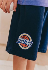 Marina basketballshorts i mjukt tyg med ett cirkulärt mönster som har en basketboll och texten "STREETBALL" i blått och orange.