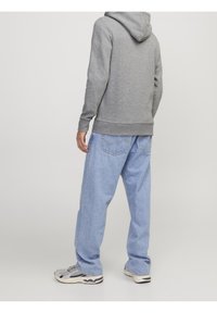 Sudadera gris con bolsillo tipo canguro, puños acanalados y capucha con cordón, combinada con jeans ligeros de corte holgado en azul claro y zapatillas grises.