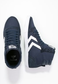 Baskets montantes navy en tissu et daim avec des accents blancs et un motif en zigzag. Comprend un col rembourré et une semelle en caoutchouc.