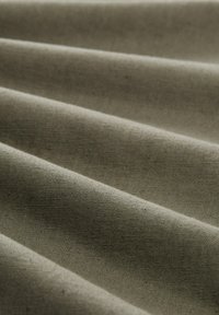 Gros plan sur un tissu doux de couleur vert olive avec une texture de tissage visible et de légers plis créant des ombres diagonales.