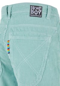 Pantaloni in corduroy verde menta con superficie texturizzata, tasca posteriore con dettaglio a strisce multicolori e un patch logo nero sulla vita.