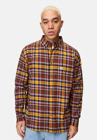 Ruutukuosisessa flanellipaidassa on burgundin, keltaisen ja purppuran sävyjä. Tässä pitkähihaisessa paidassa on napitettava kaulus ja rintatasku.