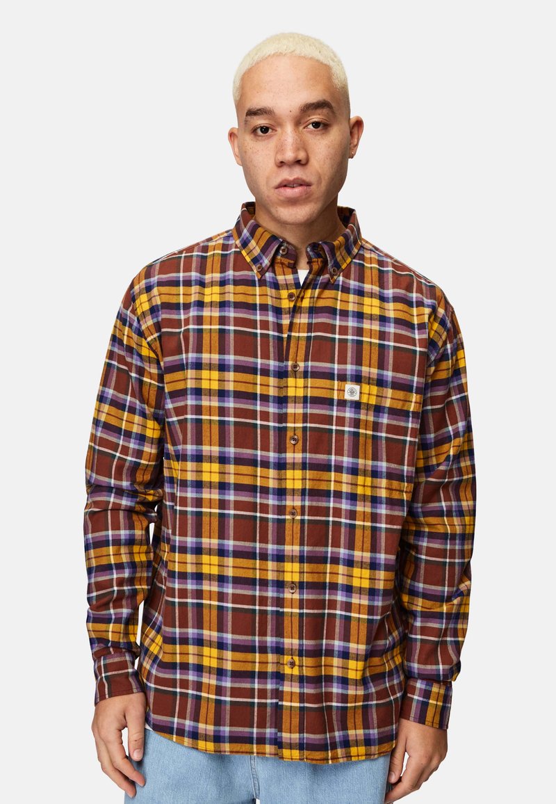 Ruutukuosisessa flanellipaidassa on burgundin, keltaisen ja purppuran sävyjä. Tässä pitkähihaisessa paidassa on napitettava kaulus ja rintatasku.