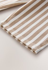 Närbild av beige och vit vertikalt randigt tyg med synliga sömmar på en ljus yta.