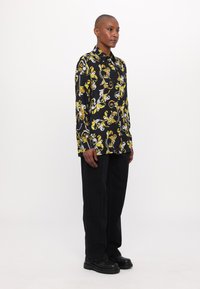 Maglietta nera a maniche lunghe con un motivo floreale giallo e bianco, design non strutturato, abbinata a pantaloni neri a gamba larga e scarpe chunky nere.