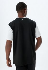 Camiseta atlética de manga corta en blanco y negro, con la parte trasera completamente negra, cuello redondo y un pequeño logo en la parte superior central de la espalda. Textura suave.