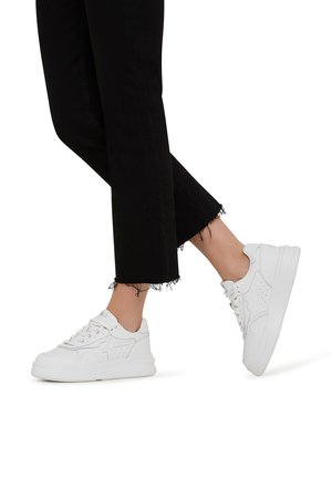 White sneakers with textured leather, perforated details, and a thick rubber sole, paired with black cropped frayed jeans.
