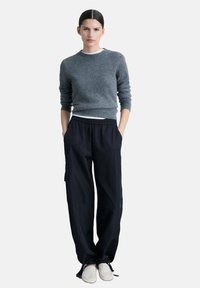 Grå stickad tröja med rund hals, i kombination med löst sittande svarta byxor och vita slip-on skor. Avslappnad och bekväm design.