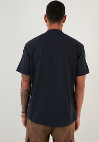 Dark navy short-sleeve shirt with a relaxed fit, subtle texture, and a curved hem. Features a standard collar and rolled sleeves.