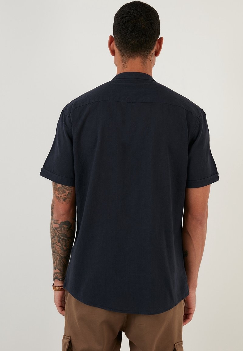 Dark navy short-sleeve shirt with a relaxed fit, subtle texture, and a curved hem. Features a standard collar and rolled sleeves.