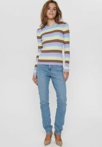 Maglione a righe striato in blu chiaro, giallo, marrone e lavanda, abbinato a jeans blu chiaro e tacchi alti color beige. Maniche lunghe, design aderente.