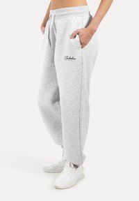 Grijze katoenen sweatpants met zijzakken, een elastische tailleband en een logo op de linker dij. Gecombineerd met witte sneakers.