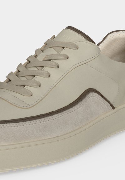 Gros plan d'une basket beige avec des panneaux en daim et en cuir, des lacets assortis et une semelle épaisse en caoutchouc avec bord texturé.