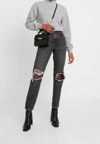 Šedá mikina na zip s fleecem; černé džíny s vysokým pasem a potrhanými koleny; černá strukturovaná kabelka; černé kotníkové boty.