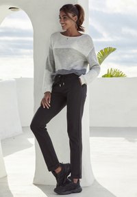 Grau-weiß gestreifter Strickpullover mit Rundhalsausschnitt, kombiniert mit schwarzen Jogginghosen mit Kordelzug und seitlichen Taschen. Schwarze Sneaker.