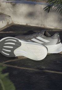 Graue Sportschuhe mit einer strukturierten Mesh-Oberfläche, weißen Akzenten und einer segmentierten Gummisohle mit Rillen für besseren Halt.