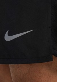 Pantalones cortos deportivos negros hechos de una tela ligera, con un logo gris de Nike en el dobladillo. Bordes sin costuras y textura suave.