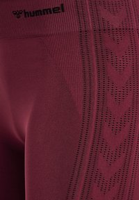 Leggings deportivos color burdeos con una cintura acanalada, que presentan un patrón texturizado de pequeños agujeros y formas de cheurón a lo largo del lateral.