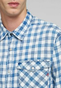 Camicia a quadri blu e bianca in cotone, con taschino sul petto caratterizzato da un accento rosso e un design con colletto classico.