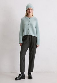 Cardigan a maglia blu chiaro con chiusura a bottoni, abbinato a pantaloni a righe scure e scarpe stringate nere, accessoriato con un berretto abbinato.