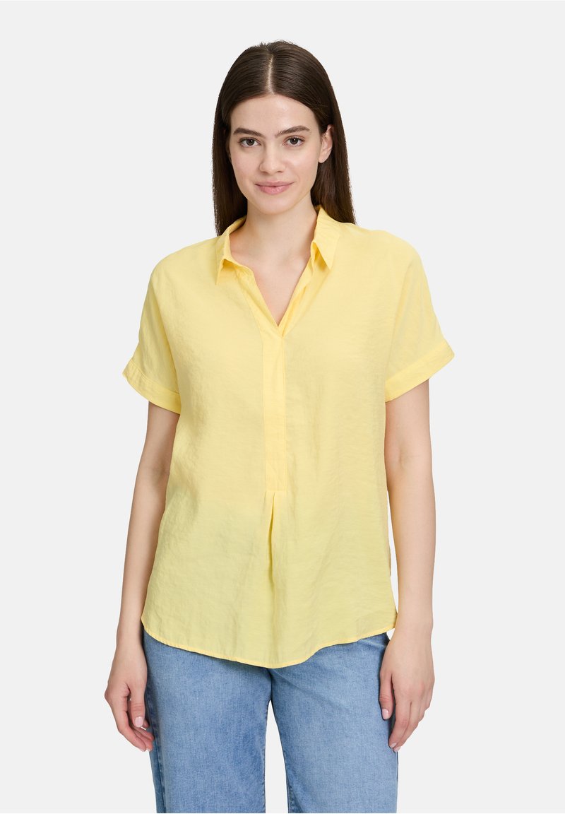 Chemise jaune à manches courtes en tissu léger, avec un col en V, une patte de boutonnage à l'avant et une coupe décontractée avec un ourlet arrondi.