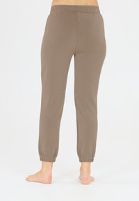 Bruine katoenen joggingsbroeken met een elastische tailleband, taps toelopende enkels en een gladde textuur, geschikt voor casual gedragen. Achtergrond is puur wit.