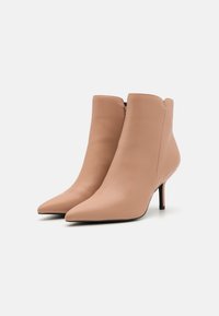 Botas de tobillo de cuero beige con punta afilada y tacón de aguja de 3 pulgadas, con una textura suave y cierre de cremallera lateral.
