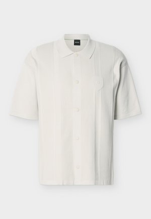 Bijela pamučna polo majica kratkih rukava s prednjim gumbima, rebrastim vertikalnim prugama, ovratnikom i suptilnim utisnutim logotipom na prsima.