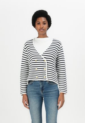 Gestreifter Cardigan in Marineblau und Weiß mit V-Ausschnitt, doppelter Knopfleiste mit goldenen Knopfakzenten und langen Ärmeln, kombiniert mit Jeans.
