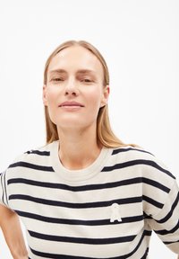 Gebreide trui met horizontale marineblauwe en roomwitte strepen, ronde halslijn en een klein wit lintaccent op de borst. Zachte textuur.