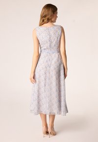 Bloemen midi-jurk in pastelblauw met roze en gele patronen, zonder mouwen ontwerp en vloeiende zoom, gecombineerd met lichtroze hoge hakken.