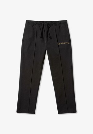 Melni bikses ar elastīgu jostu un auklu. Iespēju sarakstā ir divas sānu kabatas, priekšējie krokas un zeltīta teksta uzraksts "PAS DE MONACO."