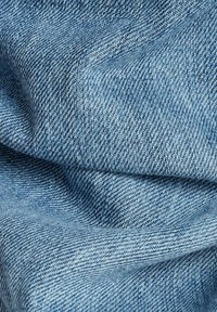 Světle modrá denimová látka s hladkým povrchem, ukazující tkaný vzor a jemné variace barev. Měkký, splývavý vzhled.