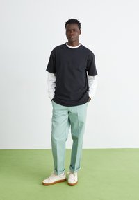 Black cotton t-shirt layered over a white long-sleeve shirt, paired with light mint green trousers and white sneakers. Simple design, casual look.