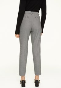 Pantalon à motifs pied-de-poule noir et blanc avec jambes droites, poches plaquées et taille haute, accompagné de chaussures noires.