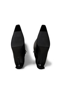 Zapatos de tacón alto negros con diseño de punta puntiaguda y acabado suave. Presentan un diseño de tacón dividido y acentos minimalistas. Suela plana.