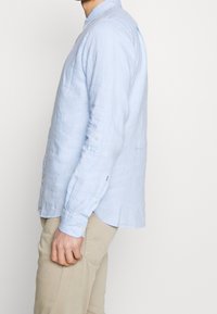 Himmelblaues Leinenhemd mit langen Ärmeln, Knopfmanschetten und klassischem Kragen. Es hat eine entspannte Passform und ein abgerundetes Saumdesign.