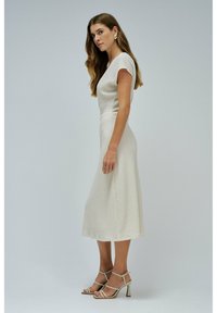 Bílé šaty po kolena z texturované tkaniny s krátkými rukávy, doplněné o béžové sandály na tenkém podpatku. Jednoduchý a elegantní design.