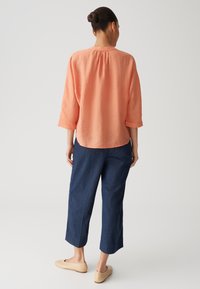 Blusa di corallo morbida con maniche a tre quarti, abbinata a pantaloni cropped blu scuro e scarpe beige slip-on. Design semplice e tessuto testurizzato.