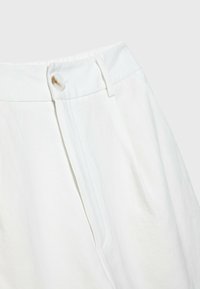 Pantaloni bianchi a vita alta con chiusura a bottone, pieghe sulla parte frontale e un tessuto morbido e texture. Nessuna tasca visibile.