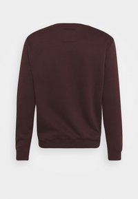 Burgundy sweatshirt med rund halsringning, långa ärmar och ribbade muddar. Slät textur med en fyrkantig applikation på övre ryggen.