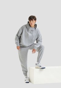 Set di felpa grigia con cappuccio e pantaloni della tuta in tessuto morbido, con una vestibilità rilassata, cappuccio regolabile, polsini elasticizzati, abbinato a sneakers bianche.
