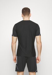 Zwart sportt-shirt van een gestructureerde stof, met korte mouwen en witte accentstrepen op de schouders.