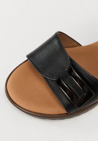 Black leather sandal featuring a wide strap with a shiny black buckle, brown textured footbed, and a smooth, rounded outsole.