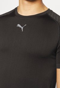 Svart idrottströja i stretchigt material, med korta ärmar och rundad hals. Silverfärgad Puma-logga på bröstet, subtila texturerade axelaccenter.