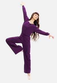 Lila dansoutfit med långa ärmar och vida byxor, tillverkad av ett mjukt material, utformat för att möjliggöra enkel rörelse.