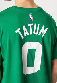 Zelené bavlněné tričko s nápisem "TATUM" bílými písmeny a číslem "0" pod ním, s visačkou NBA na horní zadní straně. Hladká textura, kulatý výstřih.