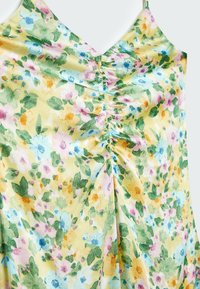 Robe florale en tissu léger, avec un fond jaune et des fleurs multicolores. Col en V et détails froncés au centre.